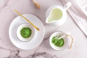 Top view of a marble table with bowls of green organic matte tea powder. a jug of milk for making a latte, a measuring bamboo spoon. photo