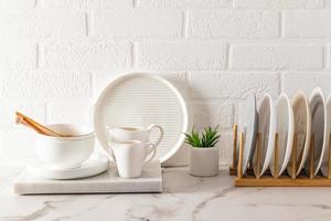 a set of kitchen utensils on a white marble countertop, a dryer with plates against the background of a white brick wall. ecologically clean house.