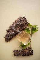 una botella sin nombre de perfume masculino o agua de tocador entre la corteza marrón de un árbol y una rama con hojas verdes. presentación de aromas. vista vertical