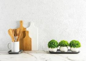 Stylish white kitchen background with various cutting boards and cooking spoons, green plants in pots on a marble countertop. photo