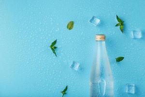 A bottle of ice water, ice cubes, drops and mint leaves on a blue background. photo