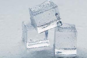 cubos de hielo en forma de pirámide con gotas de agua cerca - en macro sobre un fondo blanco. foto