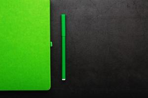 Green Notepad with a felt-tip pen on a black background, top view. photo