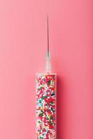 Medical Syringe filled with colorful balloons on a pink background with free space. photo