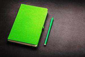 Green Notepad with a felt-tip pen on a black background, top view. photo