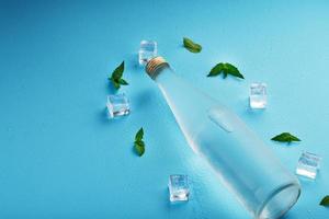 A bottle of ice water, ice cubes, drops and mint leaves on a blue background. photo