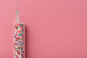 Syringe with colorful balloons on a pink background with free space. photo