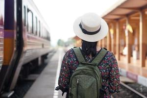 Back view of woman traveller at railway station, wear white hat and backpack. Concept, travel by train in Thailand . Transportation. Alone journey. Weeken, holiday or vacation trip. photo