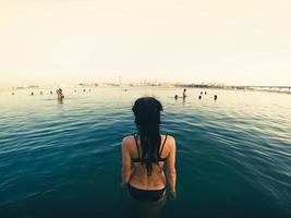 vista posterior joven mujer caucásica ingresa al agua de mar para nadar en un día caluroso en el parque aquaventure de los emiratos árabes unidos en la playa privada del hotel atlantis foto