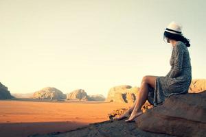 Cute young dreamy woman traveler barefoot sit viewpoint enjoy calm morning in Wadi rum desert in Jordan.Vintage travel carefree holiday tourism concept photo
