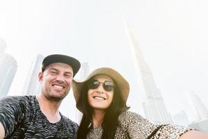 Smiling modern hippie friends couple enjoy UAE and taking picture with smartphone by Burj Khalifa on holiday vacation in sunny hot day photo