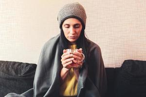 Caucasian Worried sad woman sits under blanket on sofa with cup of tea, Rising costs in private households for gas bill due to inflation and war, Energy crisis photo