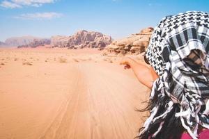 vista posterior del puesto de turista femenino ver señalar con el dedo el paisaje desértico de wadi rum en la famosa reserva natural del desierto de jordania en oriente medio. explorar jordan banner foto