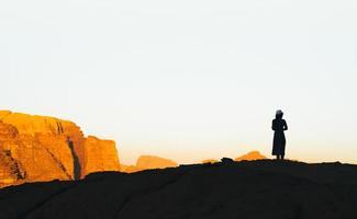 Silhouette of tourist woman on cliff greet sunrise in Jordan desert of Wadi Rum photo