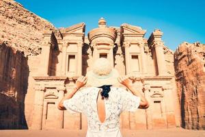 Caucasian woman tourist in white dress hold her white hat pose at Ad Deir or El Deir, the monument carved out of rock in the ancient city Petra, Jordan. UNESCO World Heritage Site photo