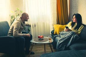 Una pareja caucásica en casa se sienta en la sala de estar y comprueba el radiador táctil de calefacción en una casa fría en Europa en el interior de su casa. temporada de calefacción y casas con calefacción de gas
