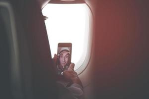 una joven pasajera caucásica posa para un teléfono inteligente con pantalla táctil selfie en el asiento de la cabina del avión antes del vuelo. chicas divertidas en publicación de vacaciones en concepto de redes sociales foto