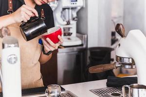 primer plano de una mujer asiática barista haciendo capuchino haciendo arte latte en una taza. foto