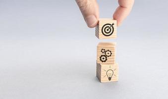 Business strategy and action plan concept. Hand putting wood block with target icon on top of others with gear and light bulb icons. Gray background. Copy space photo