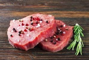 bistec de ternera cruda con romero sobre fondo de madera marrón foto