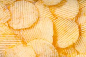 Yellow crispy ridged potato chips close up. Food background photo