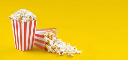 Two red white striped carton buckets with tasty cheese popcorn, isolated on yellow background photo