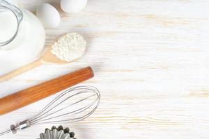 Baking ingredients flour, eggs, milk, bakeware on white wooden background with copy space photo