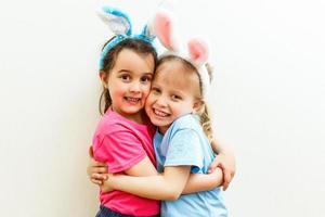 Two cute little sisters wearing bunny ears playing egg hunt on Easter. Adorable children celebrate Easter at home. photo