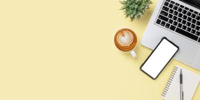 Office desk with laptop computer, Blank screen smart phone, cup of coffee, Notebook on yellow background, Top view with copy space, Mock up. photo