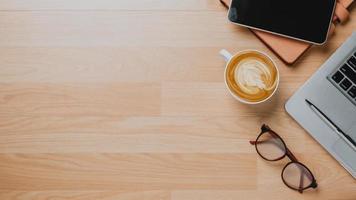 Office wooden desk workplace with laptop, tablet, pen, eyeglass, notebook and cup of coffee, Top view flat lay. photo