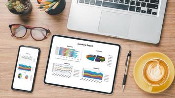 Tablet and smartphone with charts and reports on wooden desk workplace. Top view flat lay photo