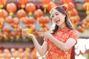mujer asiática con vestido rojo cheongsam qipao sostiene dinero de oro antiguo dentro del templo budista chino durante el año nuevo lunar para la mejor bendición y el concepto de buena suerte foto