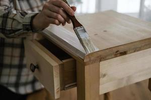 mujer pintando una mesita de noche de madera con un pincel foto