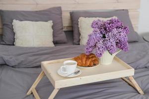 desayuno en la cama. bandeja con café, croissants y un ramo de lilas en la cama del dormitorio foto