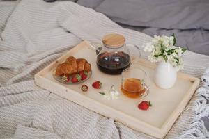 Breakfast in bed. Tray with tea, croissant and strawberries on the bed in the bedroom photo