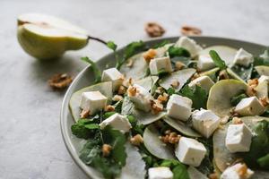 ensalada con rúcula, pera, queso feta y nueces. ensalada delicada en un plato de fondo gris foto