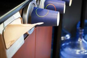 Paper cups under coffee machine in coffee shop with napkins and visible water bottles photo