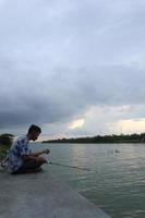 Gorontalo-Indonesia, December 2022 - A teenage boy is fishing on the riverbank in the afternoon photo