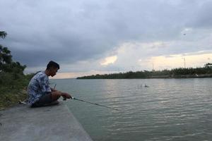 Gorontalo-Indonesia, December 2022 - A teenage boy is fishing on the riverbank in the afternoon photo