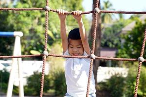 niños asiáticos jugando a la red de cuerdas de escalada en el patio de recreo. concepto de parque infantil, desarrollo infantil, deportes y recreación. enfoque suave y selectivo. foto