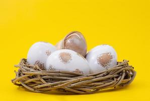 Nest with white eggs with gold on yellow background. Easter. Copy space photo