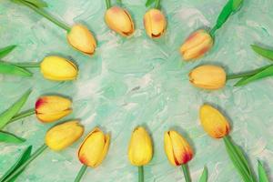 Yellow tulips arranged in a circle in the form of a frame for text on a green mint background with brush strokes. Greeting card with Easter, March 8, happy birthday, mother's day. Copy space photo