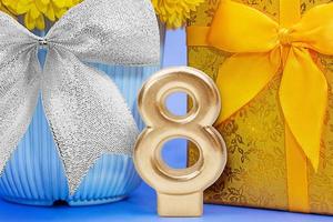 Golden number 8 with shiny yellow gift box and flower in blue pot and silver bow. International Women's Day, March 8, birthday photo