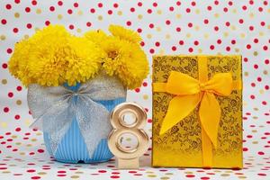 Bouquet of yellow chrysanthemums in blue pot with bow and golden gift box, number 8, behind white background with polka dots. International Women's Day, March 8, birthday photo