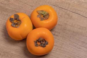 Three persimmons on wooden background photo