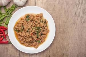 pad kaprao, pollo picado en plato blanco sobre fondo de madera foto