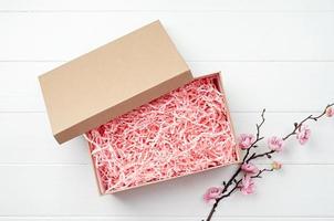 textura de material de embalaje de papel rosa triturado en una caja artesanal con rama de sakura, diseño de maqueta foto