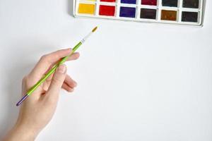 A hand with a brush reaches for watercolors. Mockup for artwork. Painting with paints photo