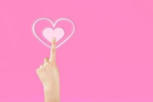 Hand on a pink background pressing on the virtual symbol of the heart. Valentine's Day photo