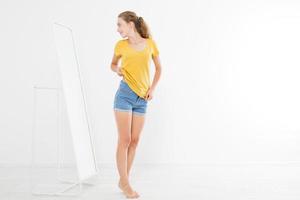 Shopping sale concept. Blonde girl in jeans and t shirt. Young woman in good body shape looking at mirror and lose weight. Copy space photo